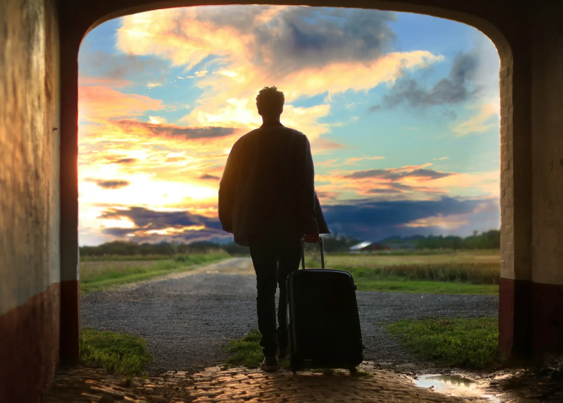 A person with a suitcase leaving through an arch into a sunset