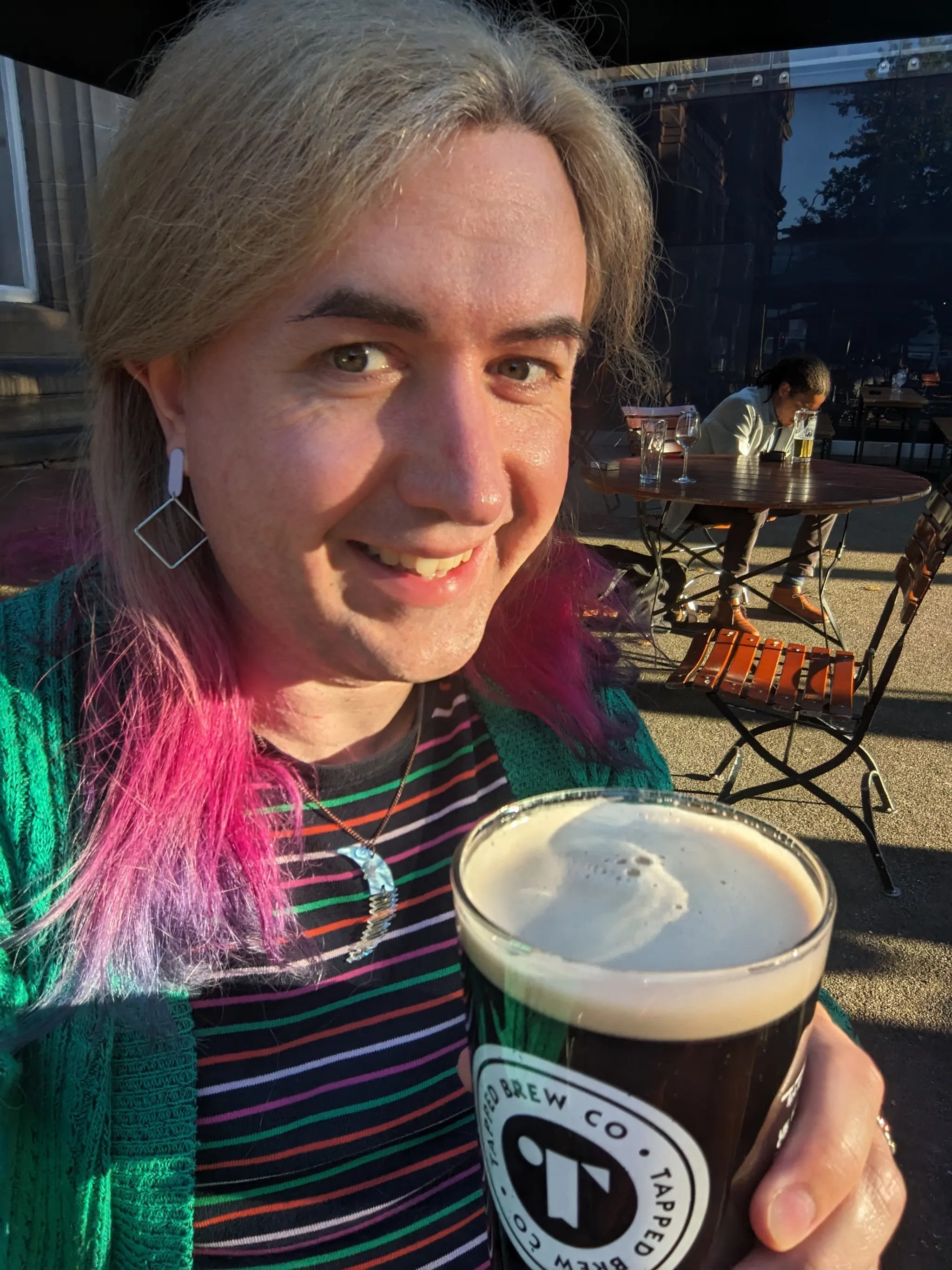 A portrait of a trans woman with colourful hair outside at a beer garden